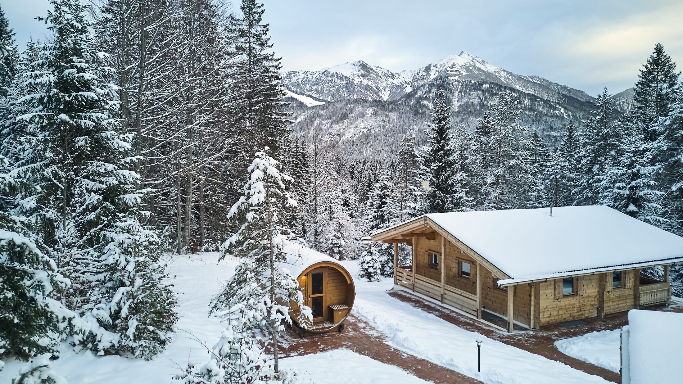 Das Chalet und die Fass-Sauna im tief verschneiten Wald mit Blick auf die Seefelder Berge